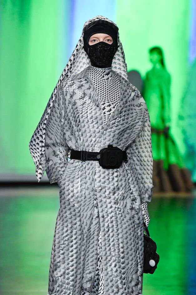 A woman wears a black and white houndstooth wrap covering her head and body, and a black mask that covers all but her eyes.